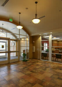Just inside the entryway of the North Dakota Veteran's Home looking at large arched wall of windows surrounding entrance doors to the left and wall of windows to the right with administration room behind.