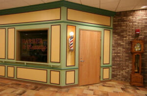 Interior of senior care building that has faux barbershop façade with barbershop sinning light and window that says "Barber & Beauty."