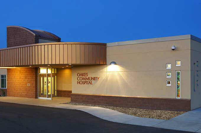 Exterior night-time view of Oakes Community Hospital with precast concrete exterior with brick and brown metal accents.