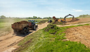 Dike reinforcement by applying a layer of clay; clay is transported by large machinery.
