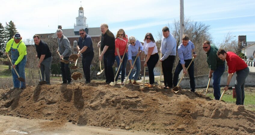 Group of people standing on sand pile shoveling scoops of sand for groundbreaking ceremony